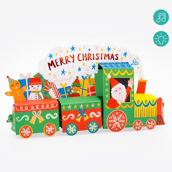 A colorful Christmas train-shaped card or craft display with multiple illustrated compartments, including Santa in the engine cab, presents, snowman and gingerbread figures, and a large 'MERRY CHRISTMAS' sign above. The product is shown on a clean white background with two teal icon graphics in the top-right corner.